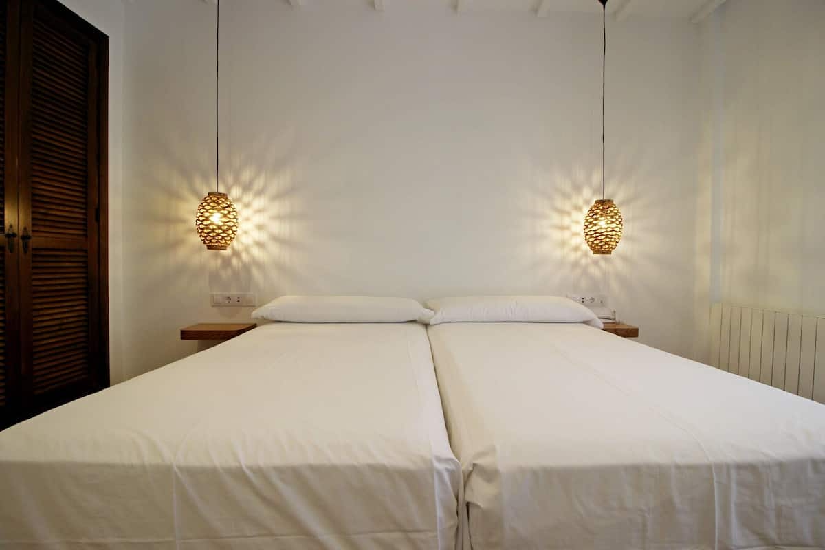 A double bed with white linens, two bedside tables, and two wall-mounted lamps.