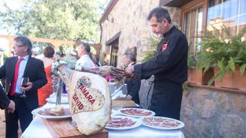 A large wheel of Parmigiano Reggiano cheese on a wooden board, surrounded by plates of cured meats, with people in the background.