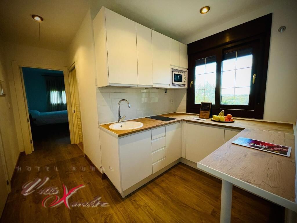 A modern kitchen with white cabinets, a wooden countertop, and a window with a view.