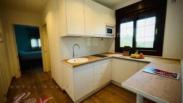 A modern kitchen with white cabinets, a wooden countertop, and a window with a view.