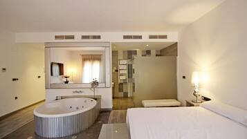 Ein modernes Hotelzimmer mit einer großen, ovalen Badewanne, einer separaten Duschkabine, einem Bett mit weißen Leinen und einem großen Spiegel über der Badewanne.