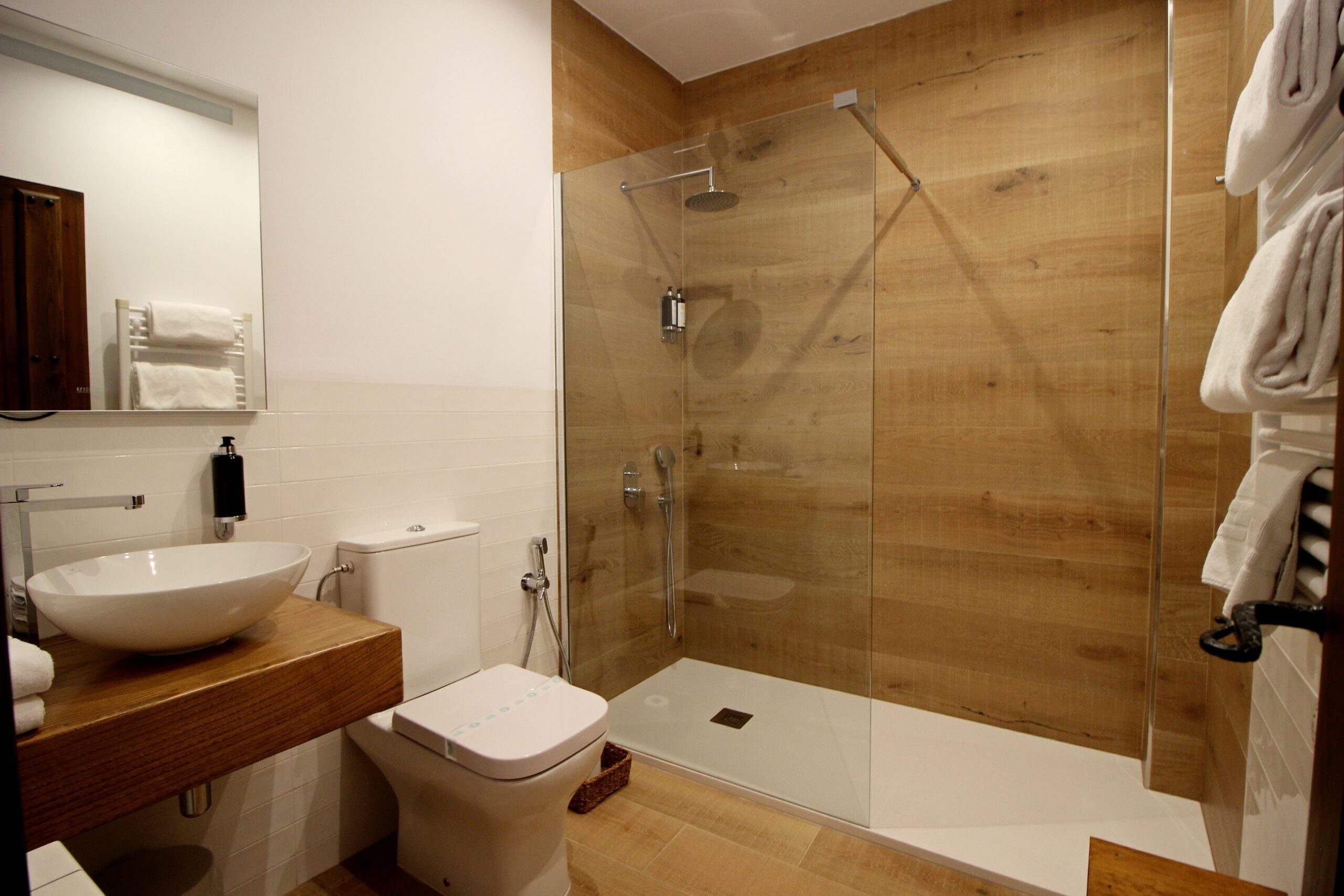Un baño moderno con ducha envuelta en vidrio, lavamanos blanco y tocador de madera.