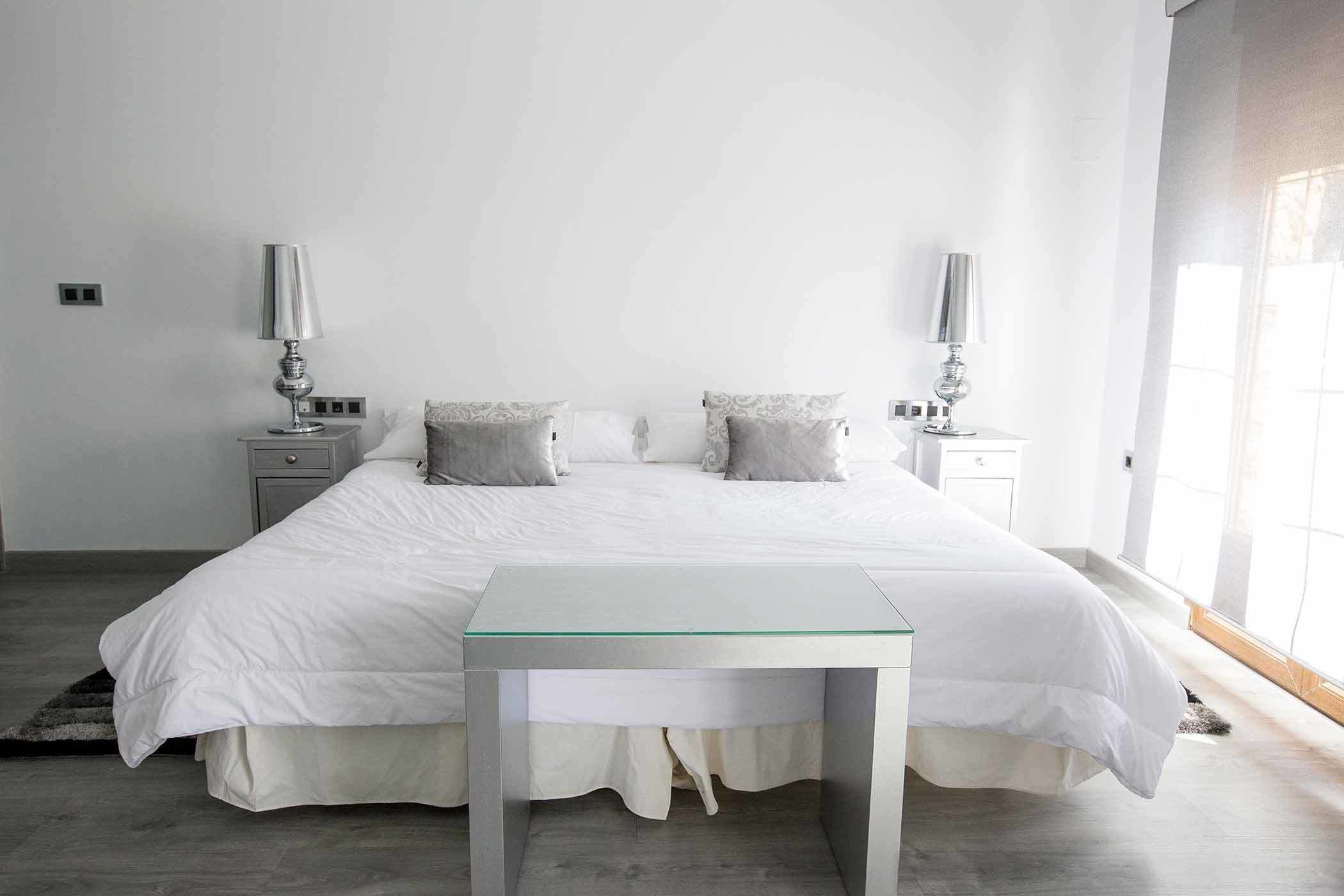 A minimalist bedroom with a large bed, two bedside tables with lamps, and a small glass table in front of the bed.