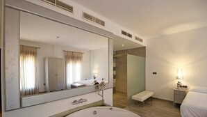 A modern hotel room with a large bathtub, a walk-in closet, a shower area, and a bedside table with a lamp. - Villa Xarahiz (Jaraíz de la Vera)