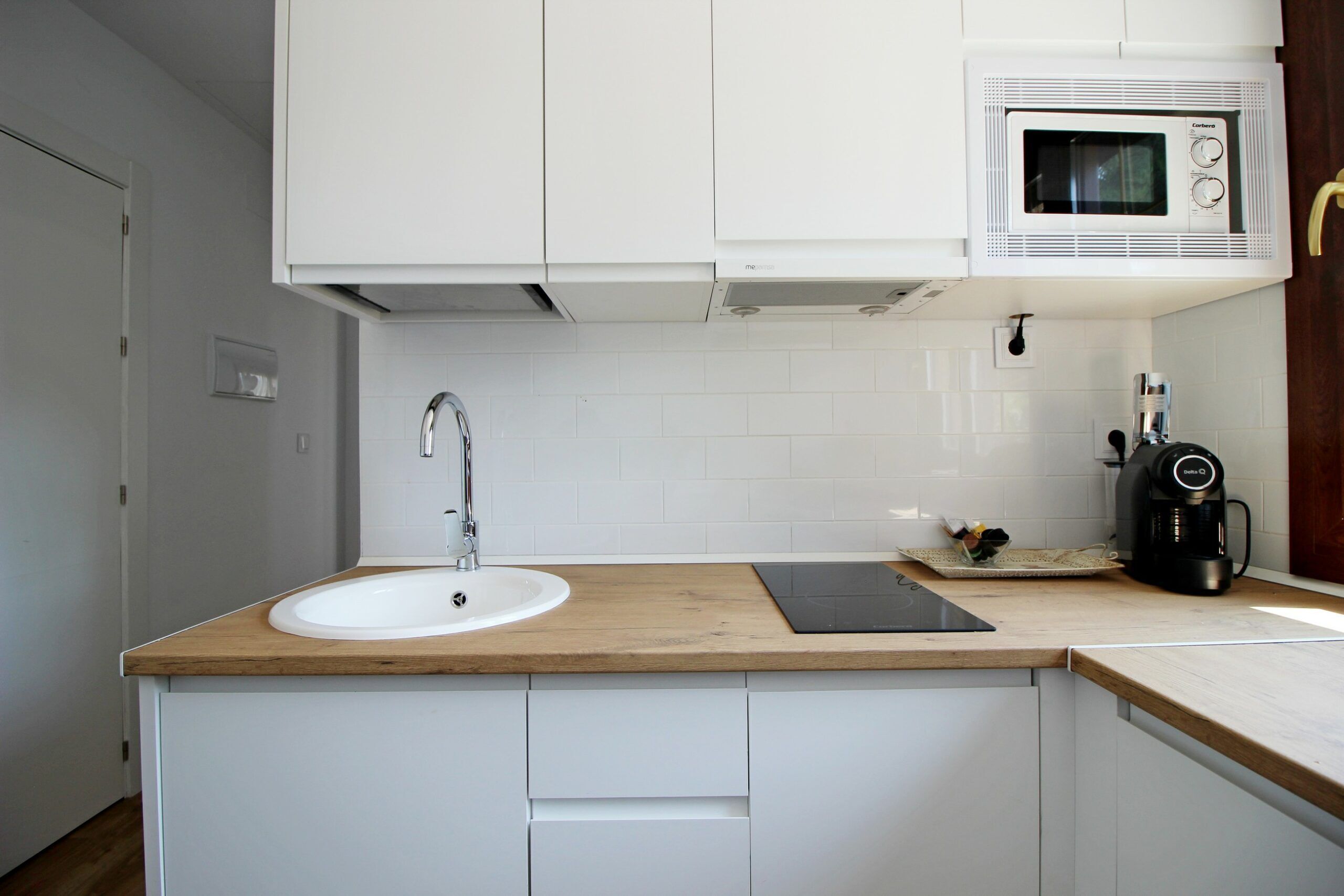 A kitchen with a wooden countertop, white cabinets, a sink, a microwave, and a coffee maker.