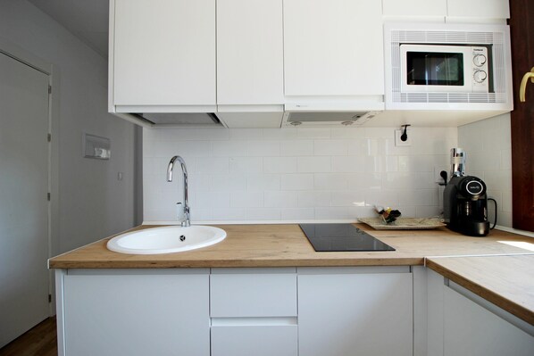 Una cocina con encimera de madera, armarios blancos, un fregadero, un microondas y una cafetera.