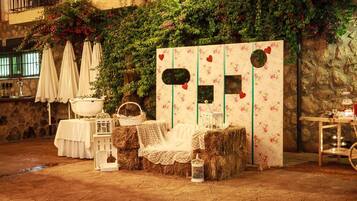 Un entorno rústico al aire libre con fardos de heno, faroles blancos y un decorado con motivos florales y corazones.