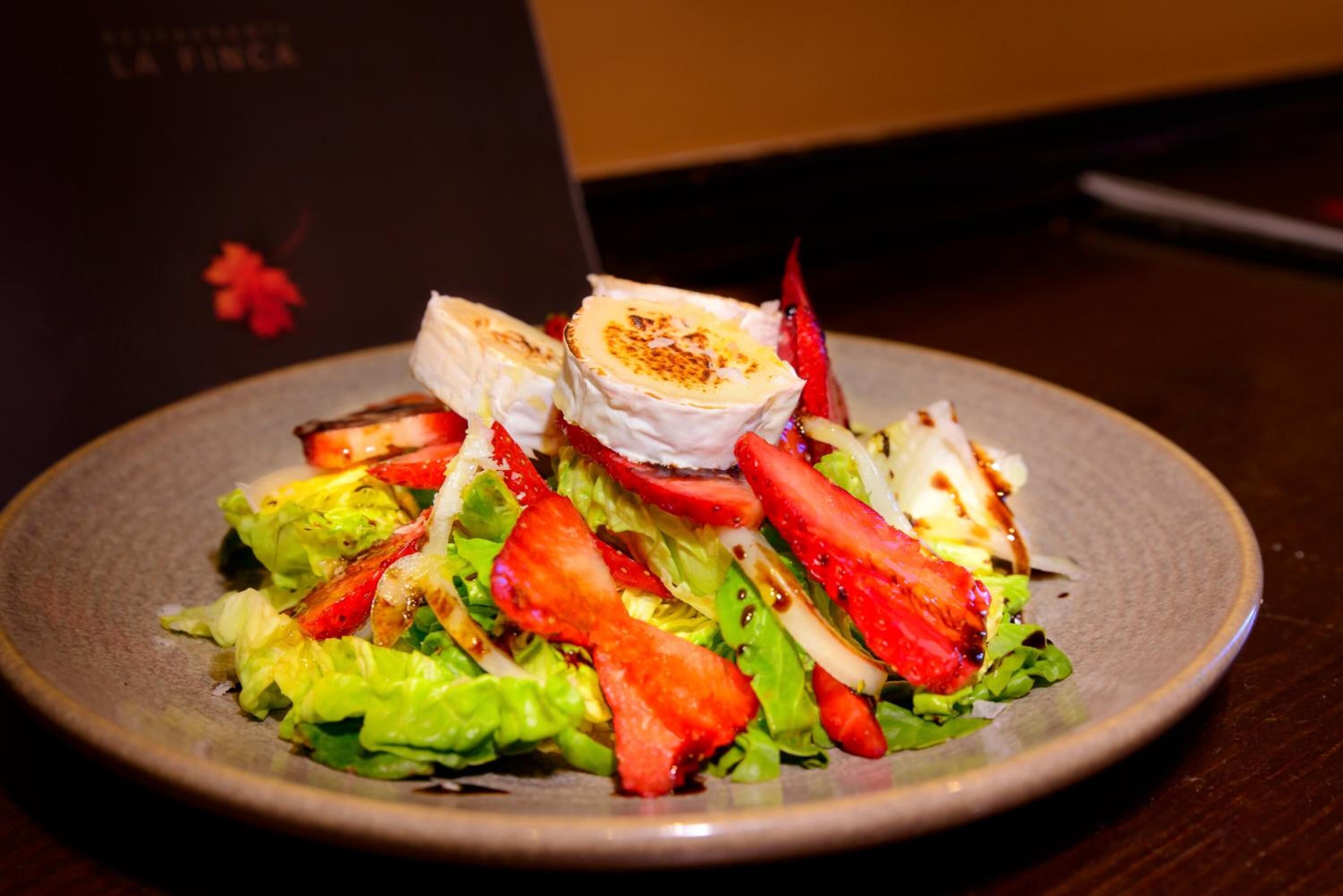 Une assiette de nourriture comprenant une salade, du poulet grillé et des fraises.