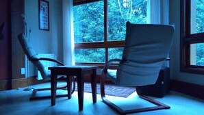 A room with a large window, a chair, a small table, and a floor lamp. - Locar-in Gramado Vista verde e perto de Tudo (Gramado)