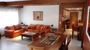 A living room with a sofa set, a coffee table, and a dining table with chairs. There is a painting on the wall and a door leading to another room. - Locar-in Gramado Vista verde e perto de Tudo (Gramado)