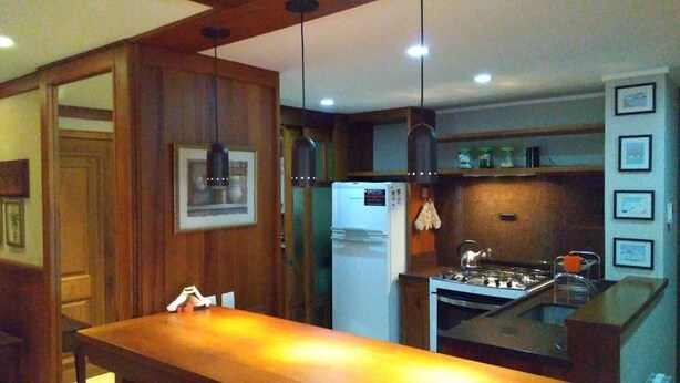 A kitchen with wooden cabinets, a refrigerator, a stove, and pendant lights. - Locar-in Gramado Vista verde e perto de Tudo (Gramado)
