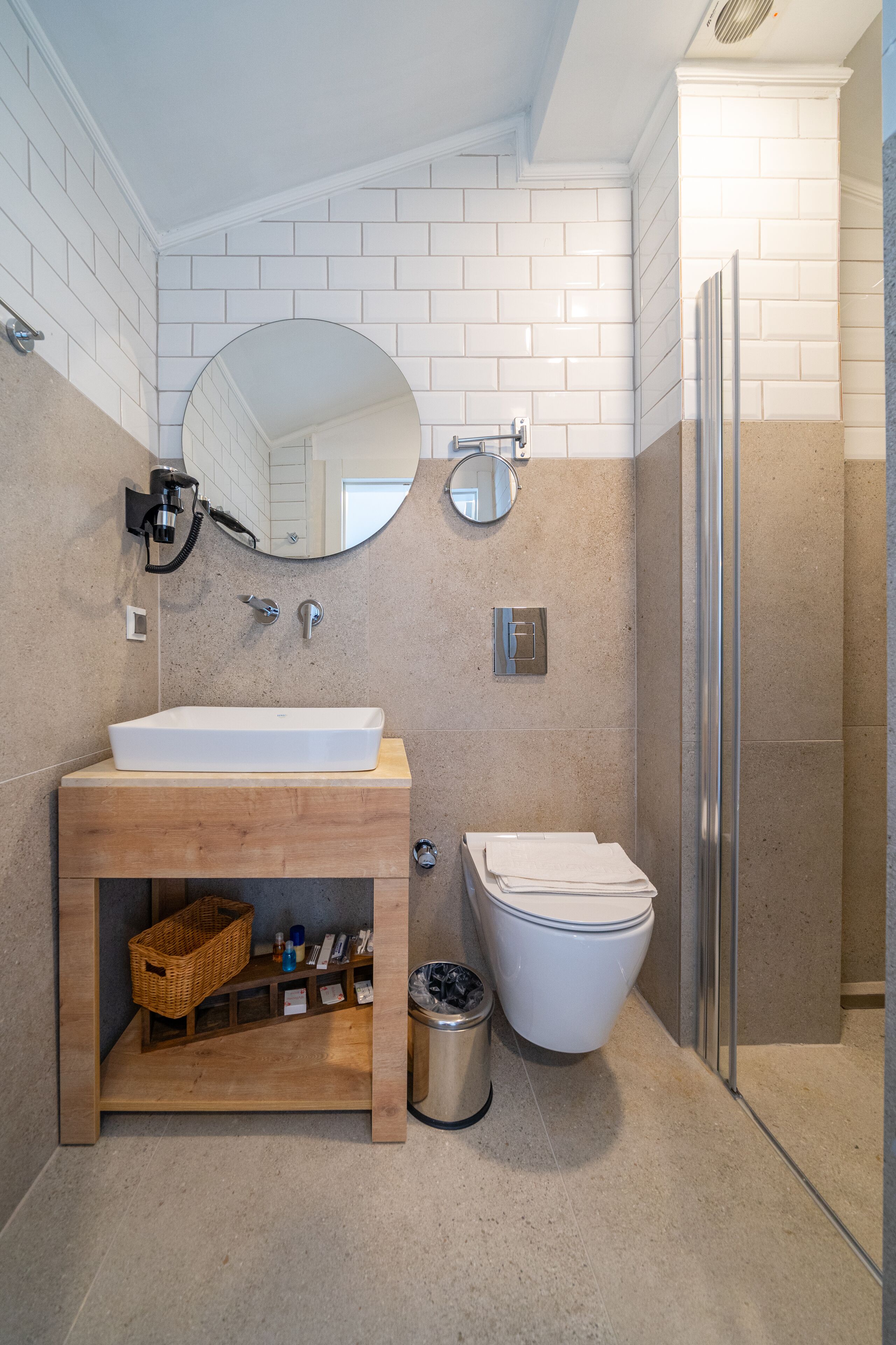A modern bathroom with a white sink, wooden vanity, a mirror, a toilet, and a shower area.