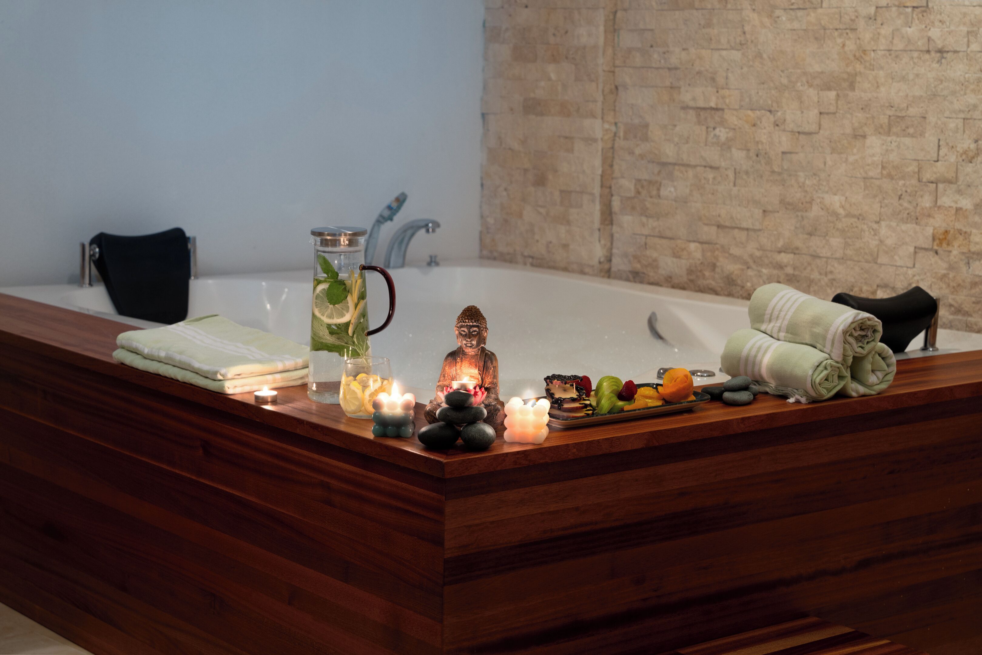 A wooden reception desk with a Buddha statue, candles, a glass of water, and a tray of fruits and vegetables.