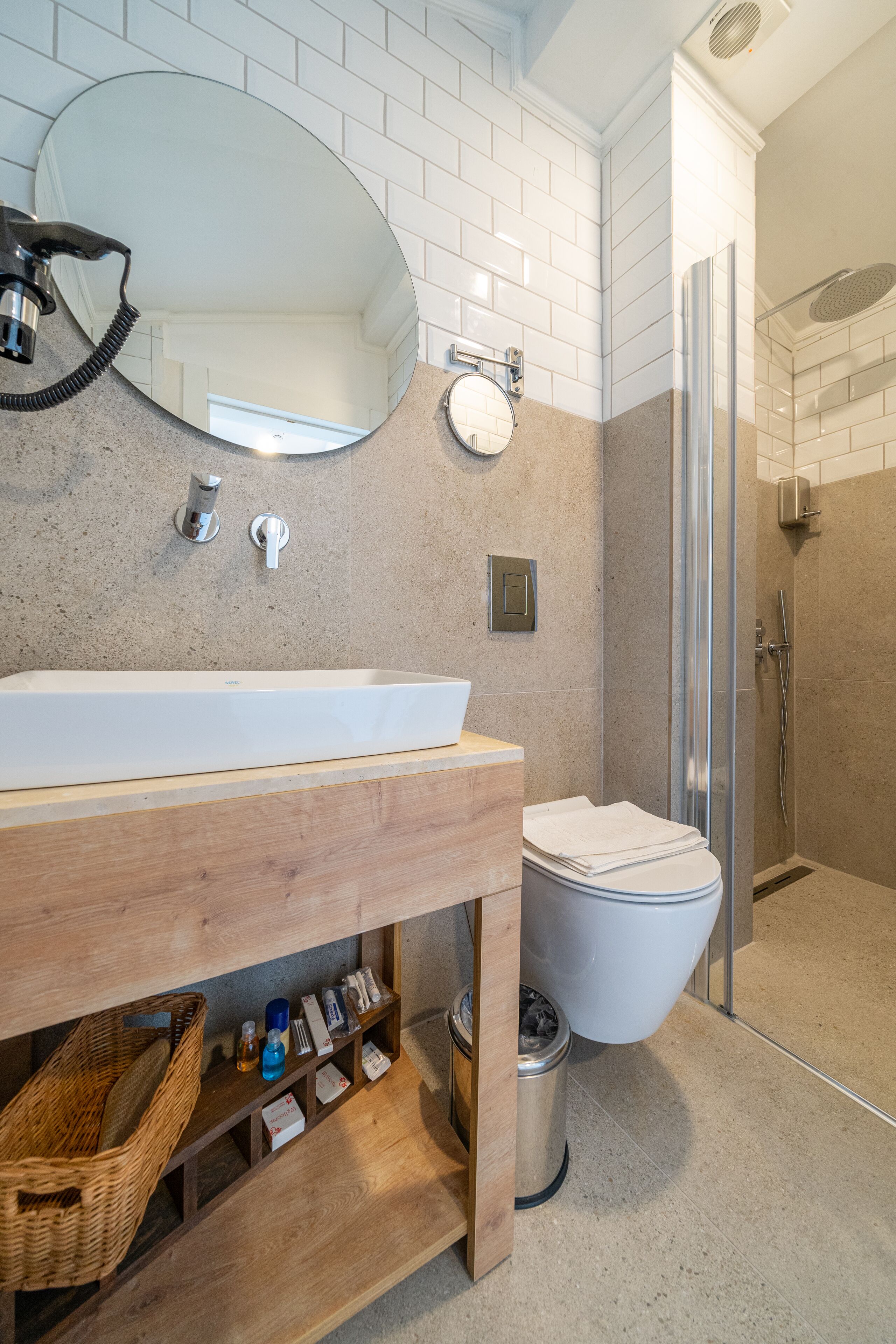 A modern bathroom with a large white sink, a round mirror, a toilet, and a glass-enclosed shower.