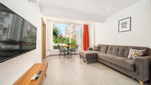 Una sala de estar moderna con un televisor de pantalla plana grande, un sofá gris, una mesa de centro de madera y un comedor con mesa y sillas.