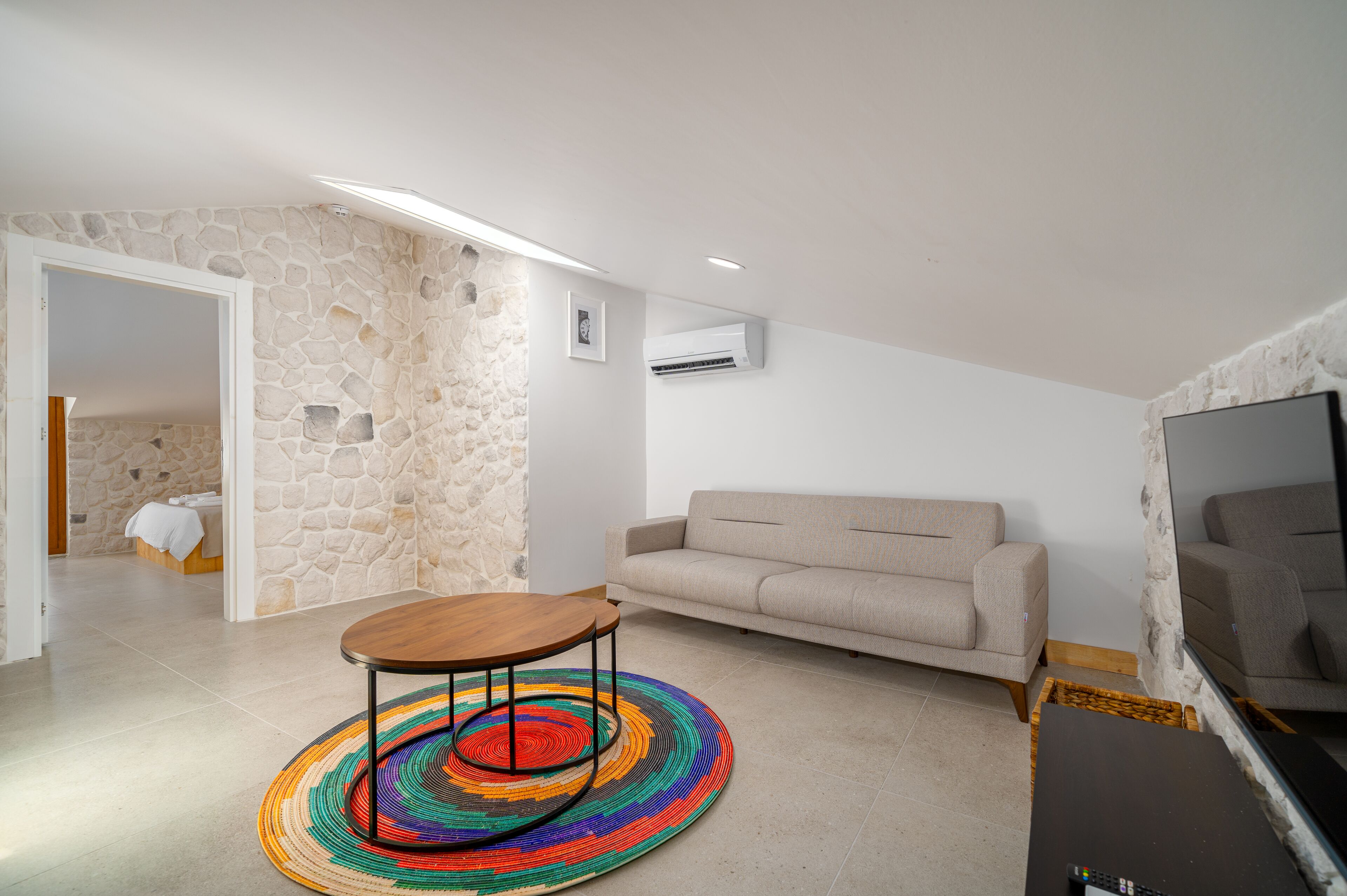 A living room with a stone wall, a beige sofa, a wooden coffee table, and a colorful rug.