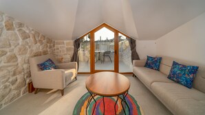 Una sala de estar acogedora con una pared de piedra, una mesa de madera y dos sofás con cojines estampados.