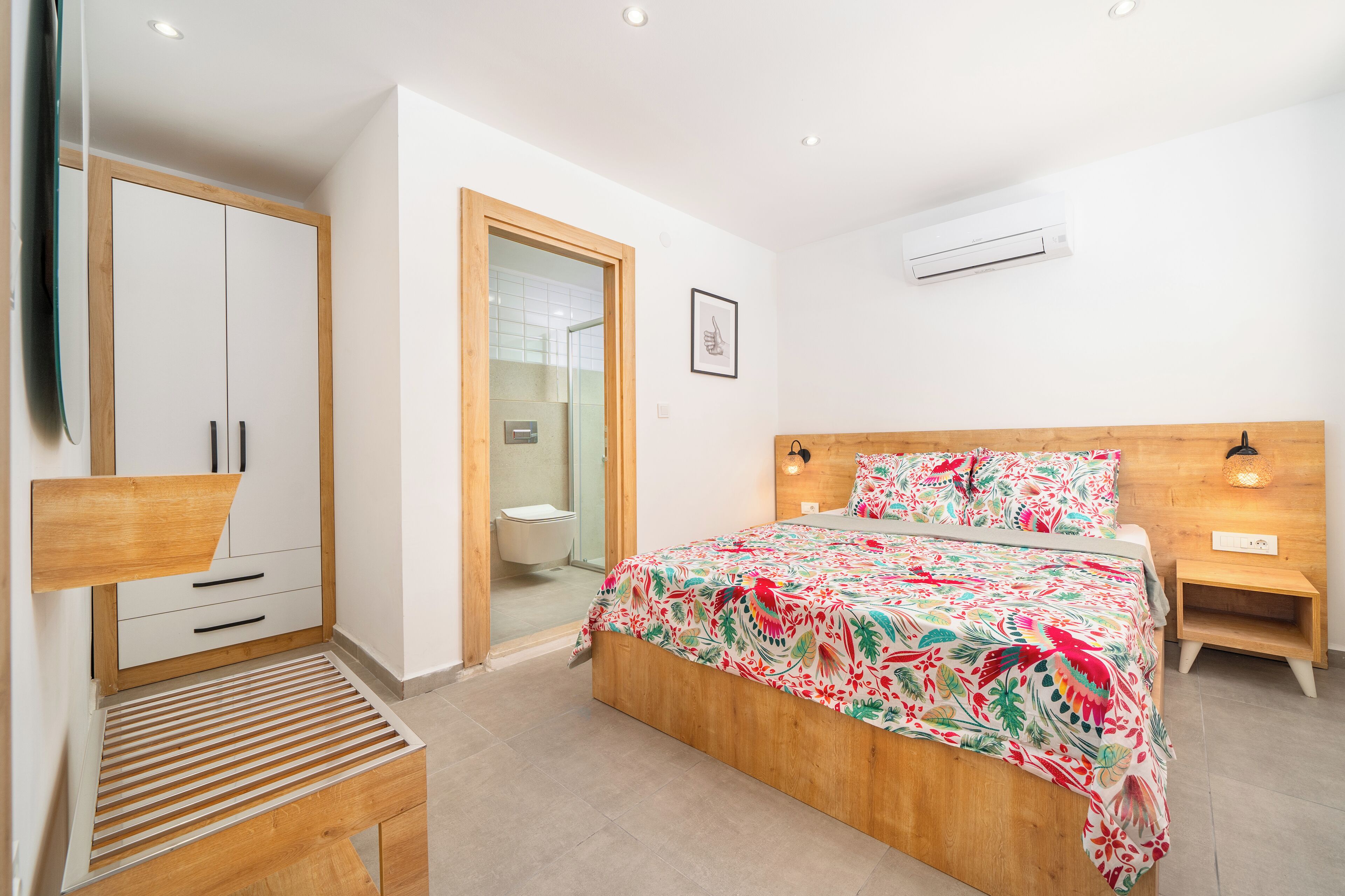 A bedroom with a bed, wooden wardrobe, bedside table, and a small stool.