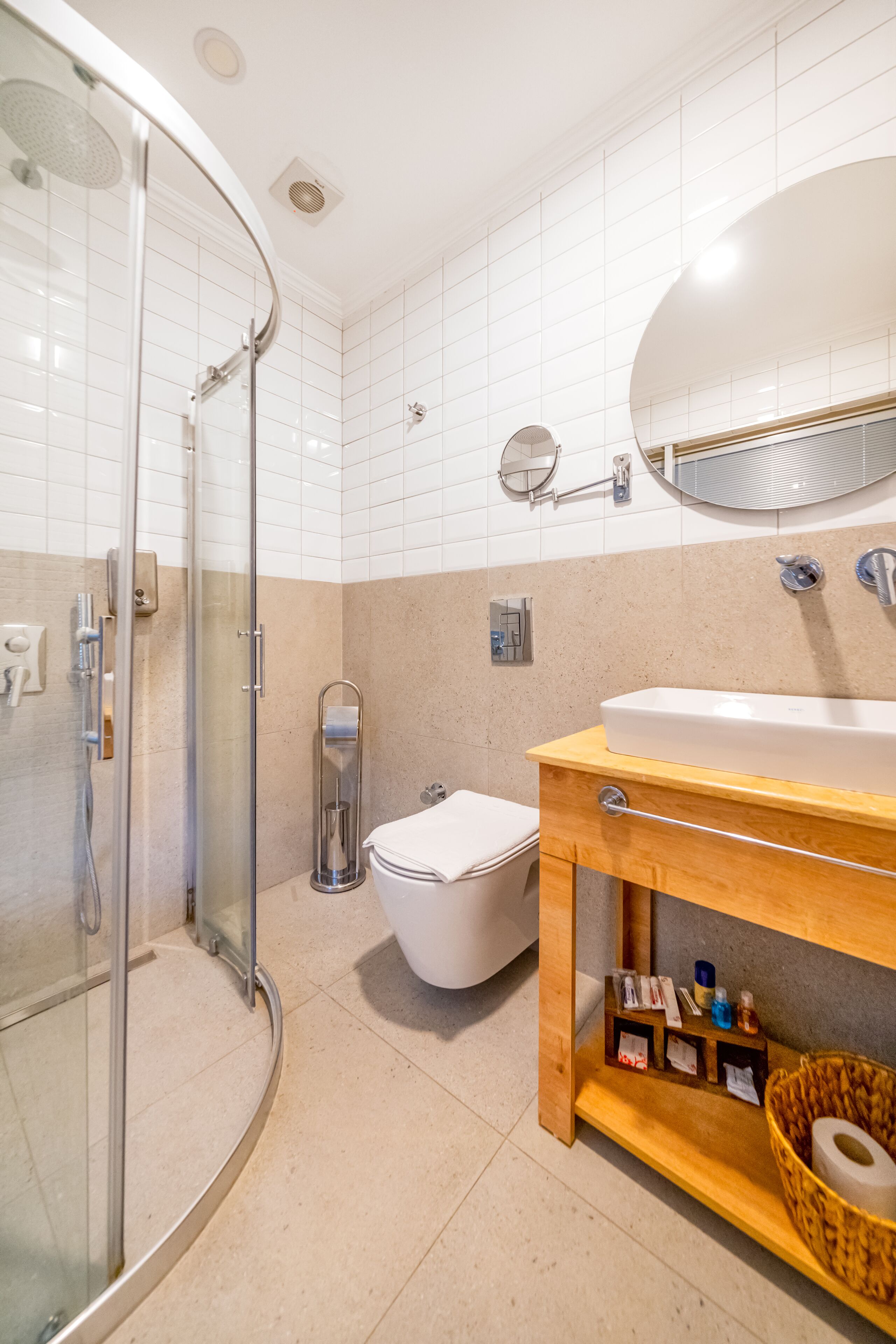 Un baño moderno con cabina de ducha de vidrio, inodoro blanco y tocador de madera con lavamanos y espejo.