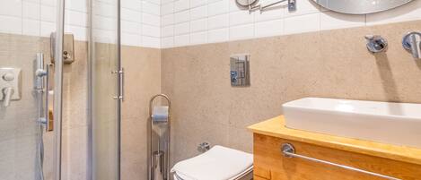 Un baño moderno con cabina de ducha de vidrio, inodoro blanco y tocador de madera con lavamanos y espejo.