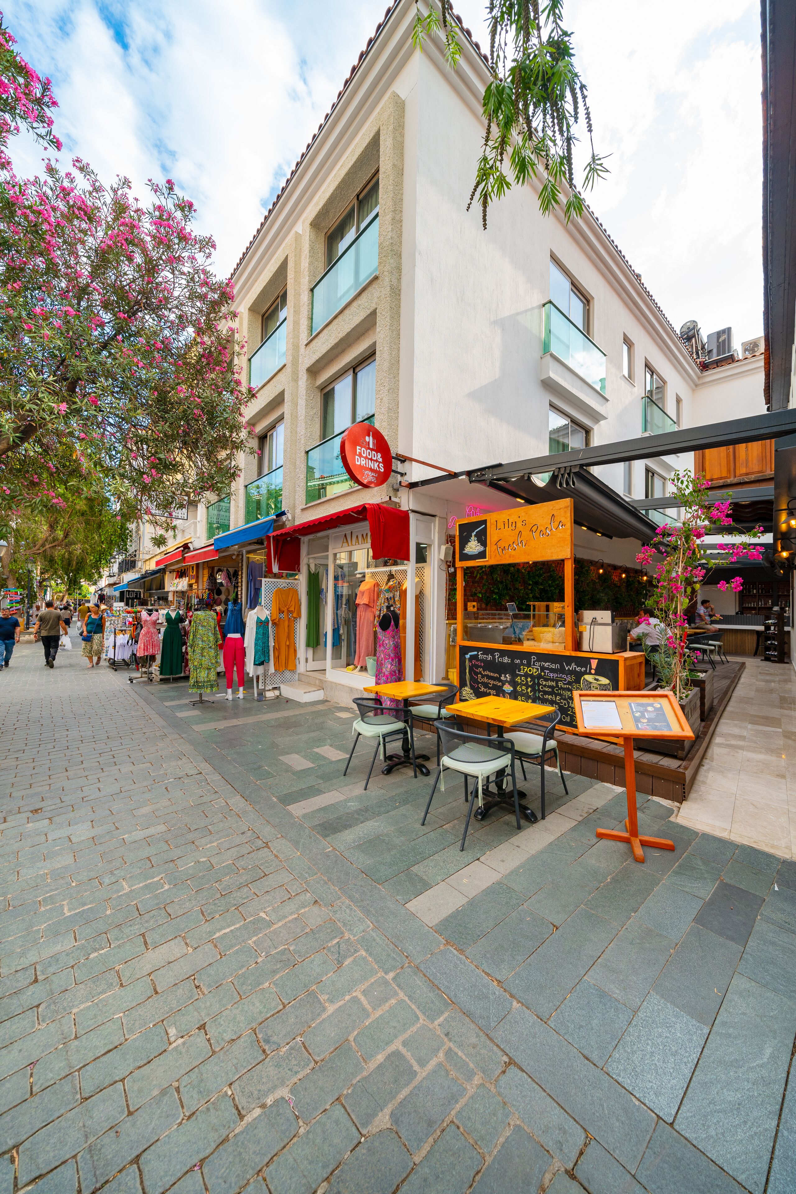 A street with outdoor seating, a food cart, and various shops.