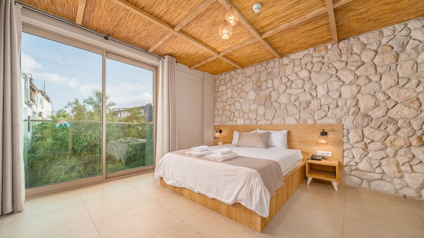 Un dormitorio con una cama grande, cabecera de madera, pared de piedra y vistas a través de un ventanal corredero.