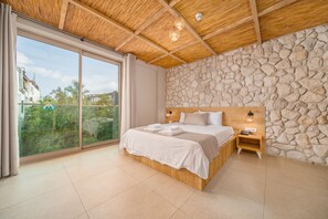 Un dormitorio con una cama grande, cabecera de madera, pared de piedra y vistas a través de un ventanal corredero.