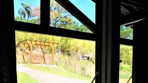 Una hamaca colgada junto a una ventana, con vista a un área cubierta de césped y una pérgola de madera.