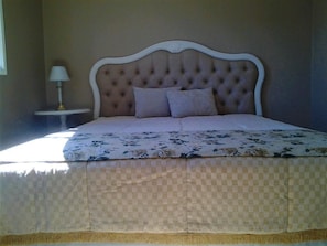 A bed with a tufted headboard, a floral bedspread, and a checkered blanket. - Casa Sol Nascente - 2 Qtos (Gramado)
