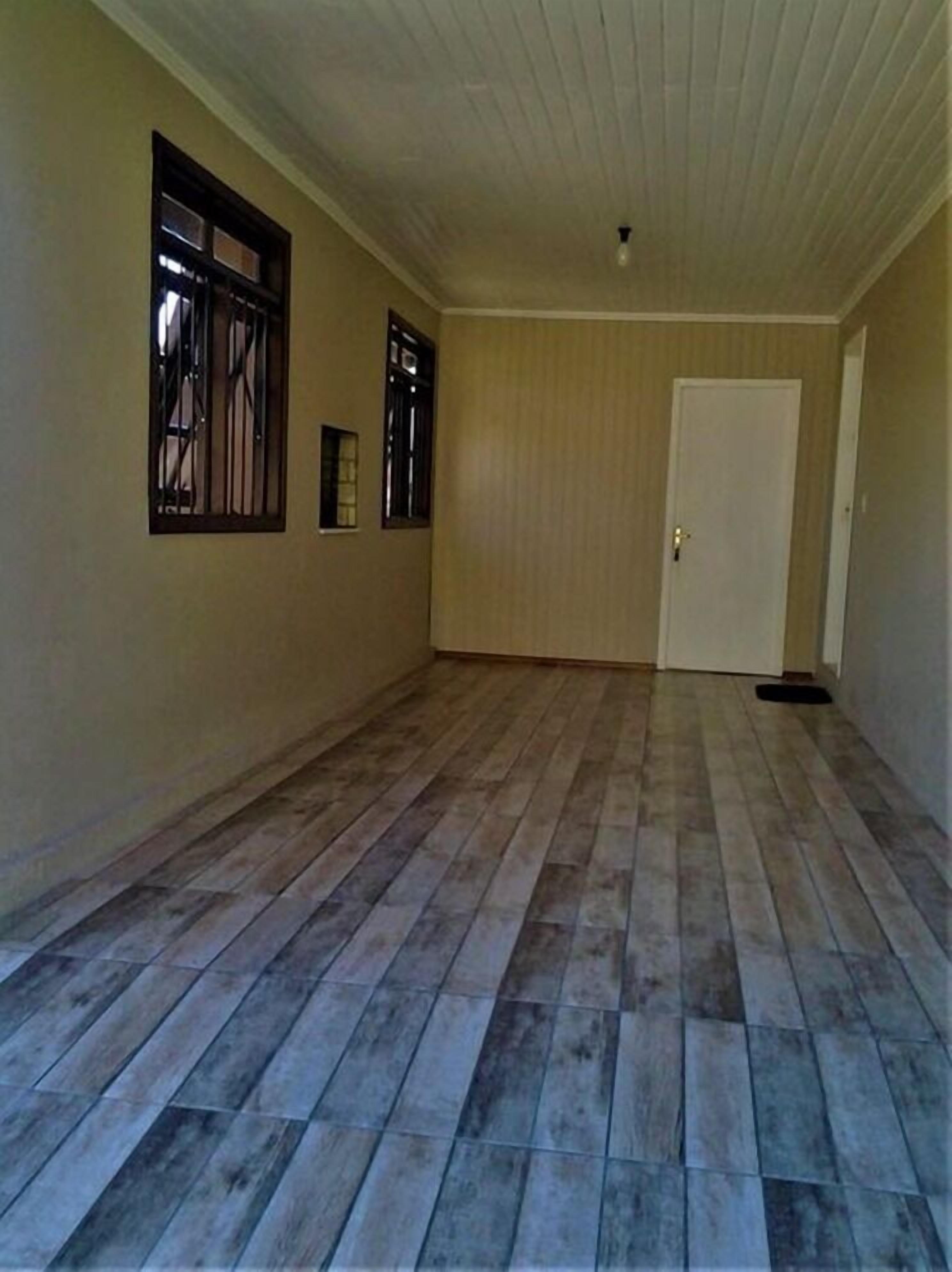 A hallway with wooden flooring, a white door, and two windows with metal bars.