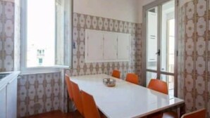 A conference room with a white table and orange chairs, patterned wallpaper, and a large window. - Dreamcatchers (La Spezia)