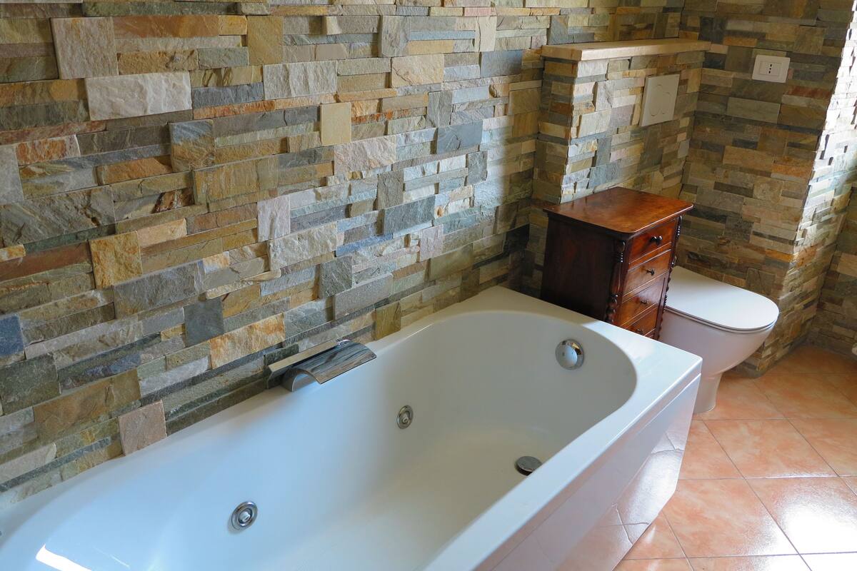 A bathroom with a stone wall, a bathtub, a wooden cabinet, and a toilet.