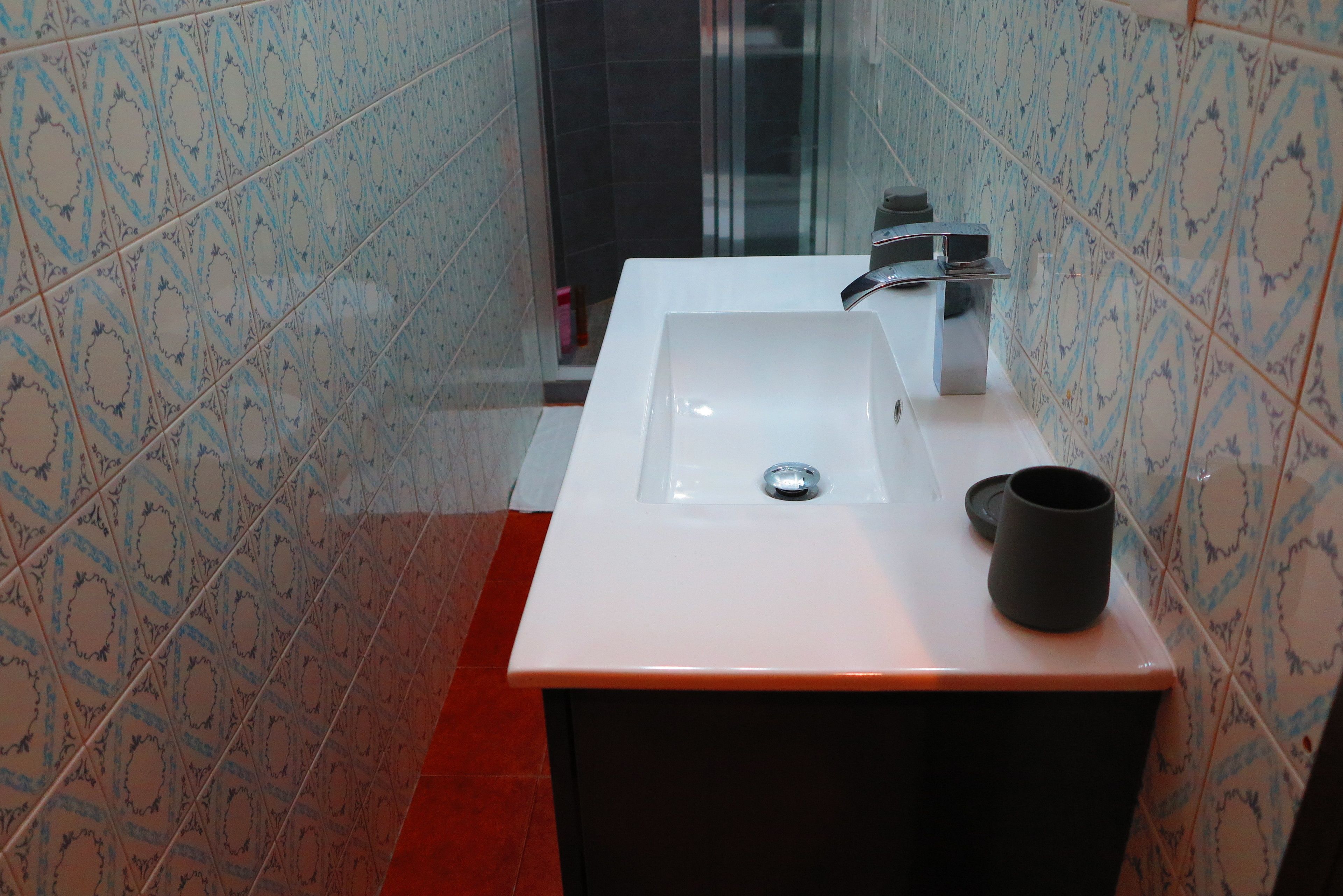 A bathroom with a white sink, black cabinet, and patterned tiles.