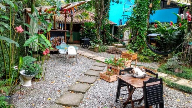 A garden with a stone pathway, a wooden table, and a chair. - Mambembe Hostel - Ilha Grande (Angra dos Reis)