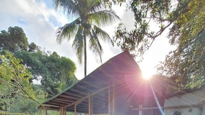 A covered outdoor area with a table and chairs, surrounded by gravel and palm trees. - Mambembe Hostel - Ilha Grande (Angra dos Reis)