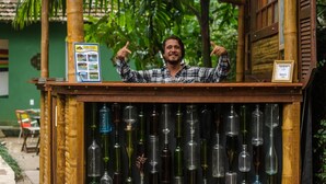A wooden kiosk with a bamboo structure, displaying various glass bottles and a poster. - Mambembe Hostel - Ilha Grande (Angra dos Reis)