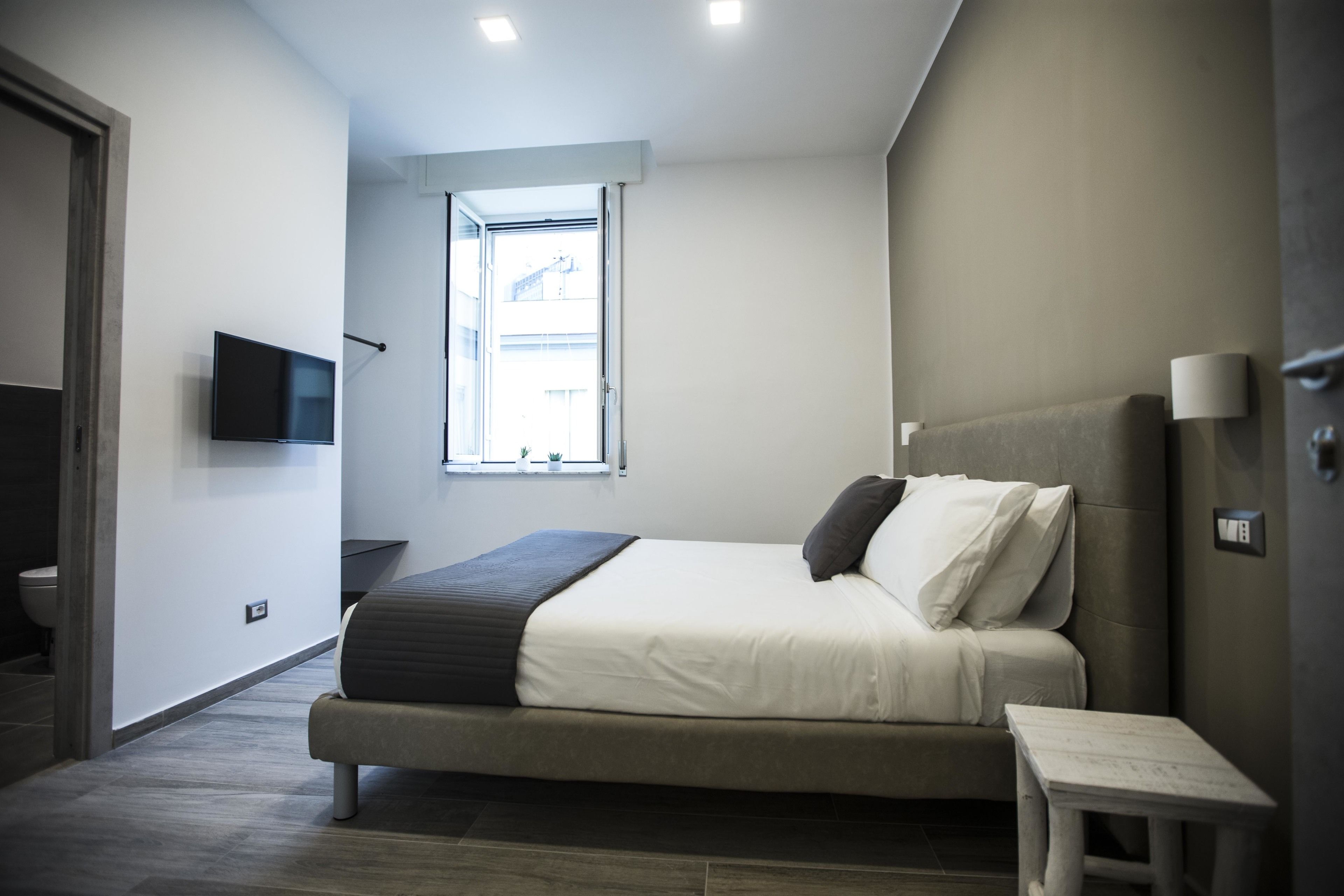 Un dormitorio moderno con una cama, una mesita de noche y un televisor montado en la pared.