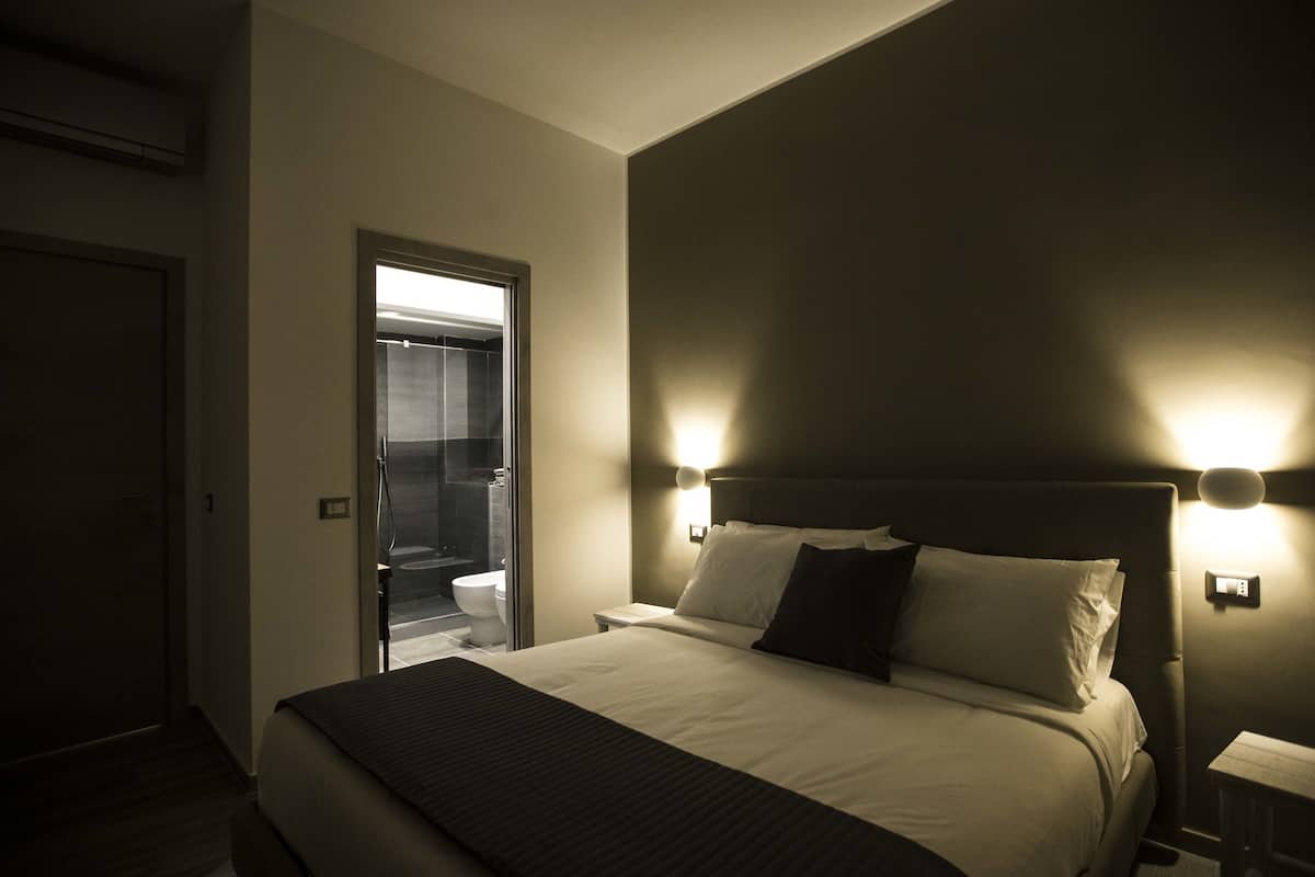 Quarto de hotel com cama, abajures, mesa de cabeceira e vista para um banheiro.