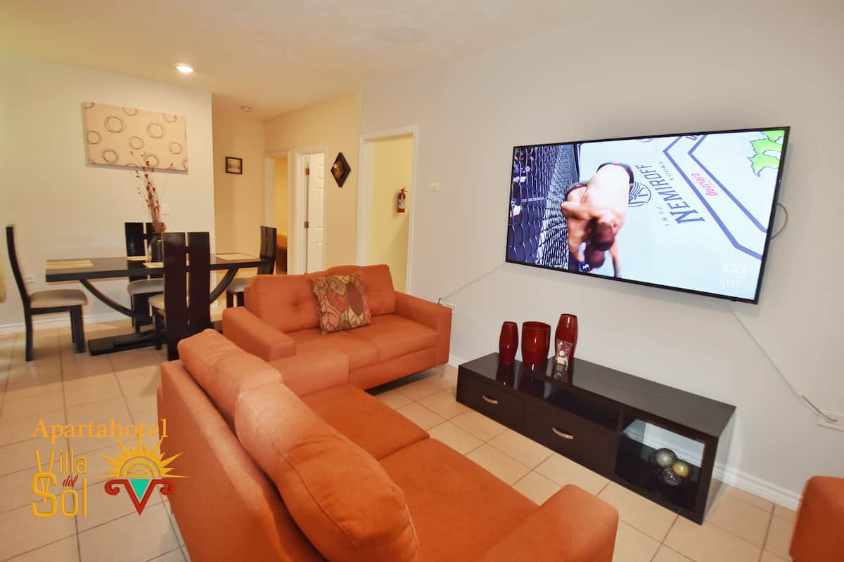 A living room with a sofa, TV, and a dining area with chairs and a table.