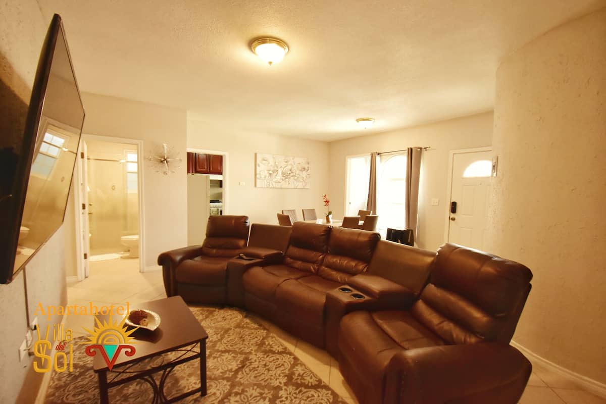 A living room with a sectional sofa, a flat-screen TV, a coffee table, and a patterned rug.
