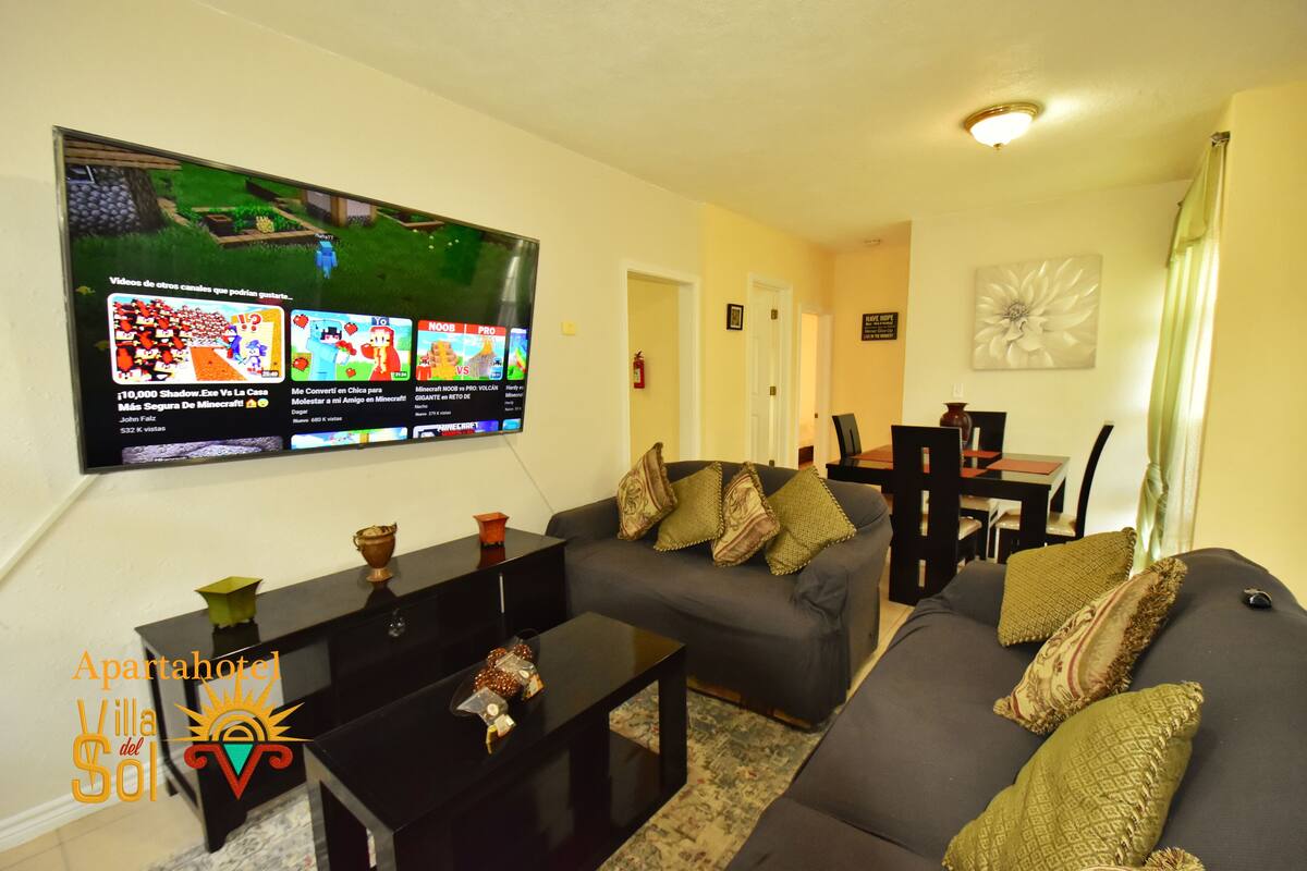 A living room with a large flat-screen TV mounted on the wall, a sofa, a coffee table, and a small side table.