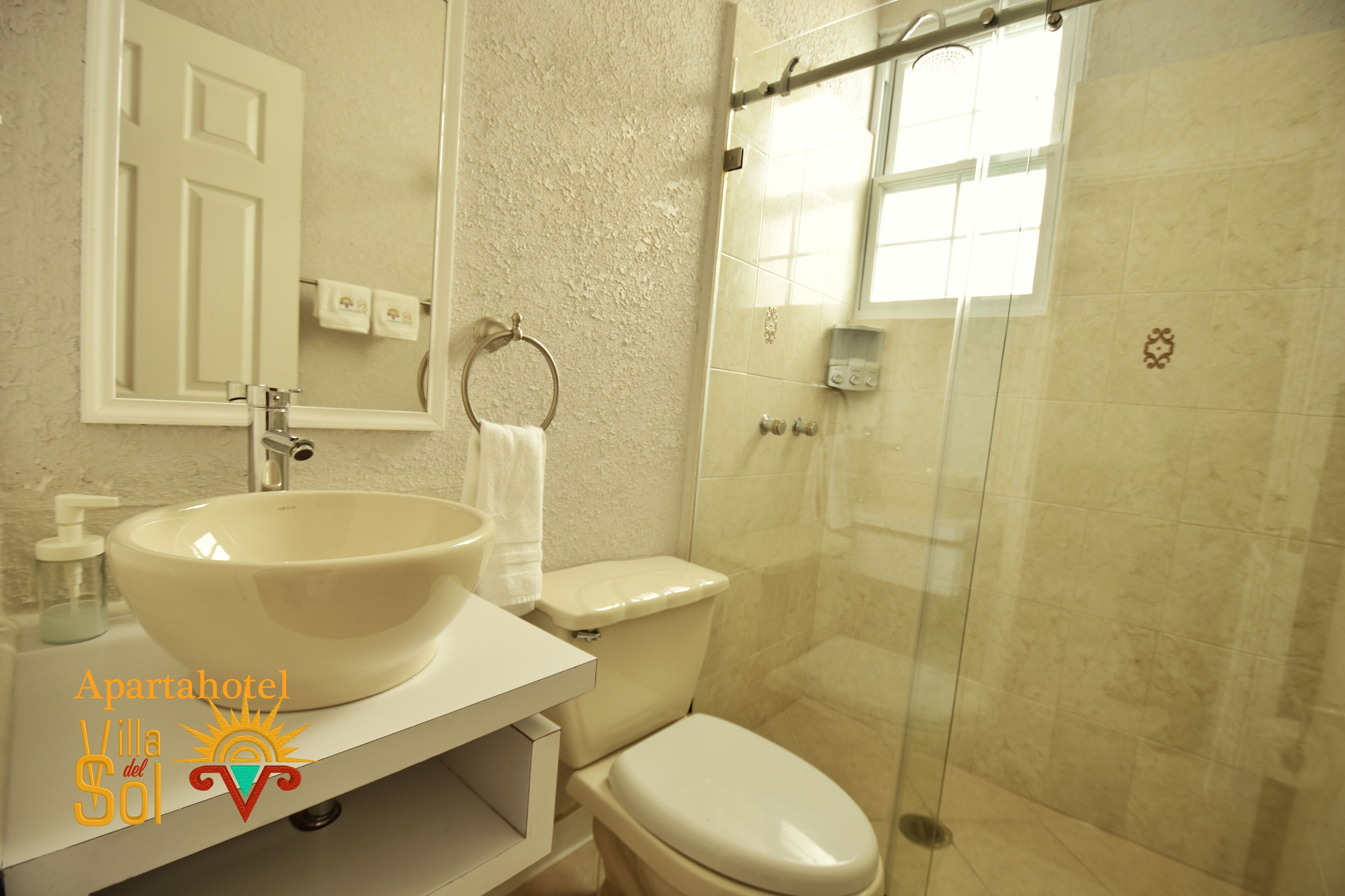 A bathroom with a large white sink, a toilet, a glass shower enclosure, and a mirror above the sink.