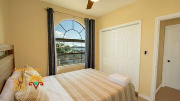 A bedroom with a bed, a window with curtains, a ceiling fan, and a door.