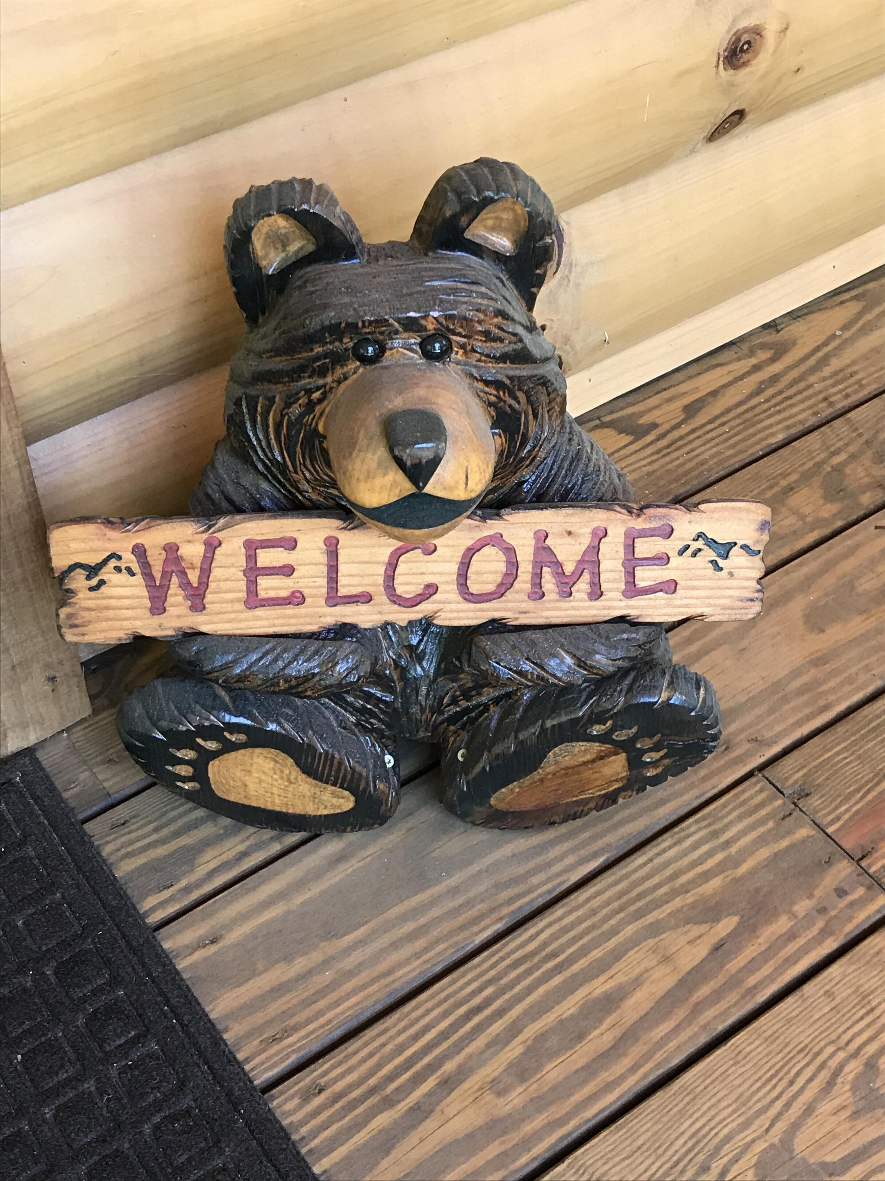 A wooden bear sculpture holding a sign that says "WELCOME".