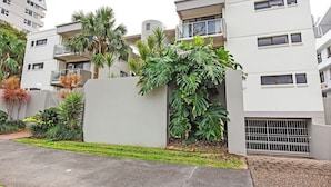 A modern apartment building with balconies, a gated entrance, and lush tropical plants. - 20 Steps to the Sand! - Beachfront Apartment! No Roads to Cross (Mooloolaba)