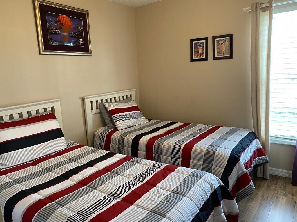 A bedroom with two beds, a window with curtains, and a framed picture on the wall.