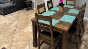 Un coin repas avec une table en bois, des chaises et un lustre. On aperçoit un canapé et une porte au fond.