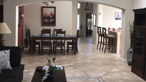 Un vaste salon comprenant un coin repas, un ventilateur de plafond et donnant sur la cuisine.