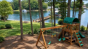 A wooden swing set and playhouse with a green roof, surrounded by trees and a lake view. - What A View! Perfect Family Meeting Place. BIG Views!  Optional Boat Rental. (Sherrills Ford)