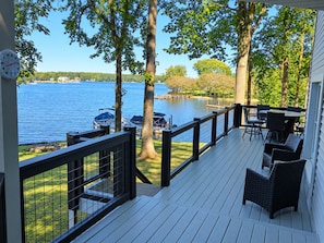A deck with a railing, outdoor furniture, and a view of a lake.